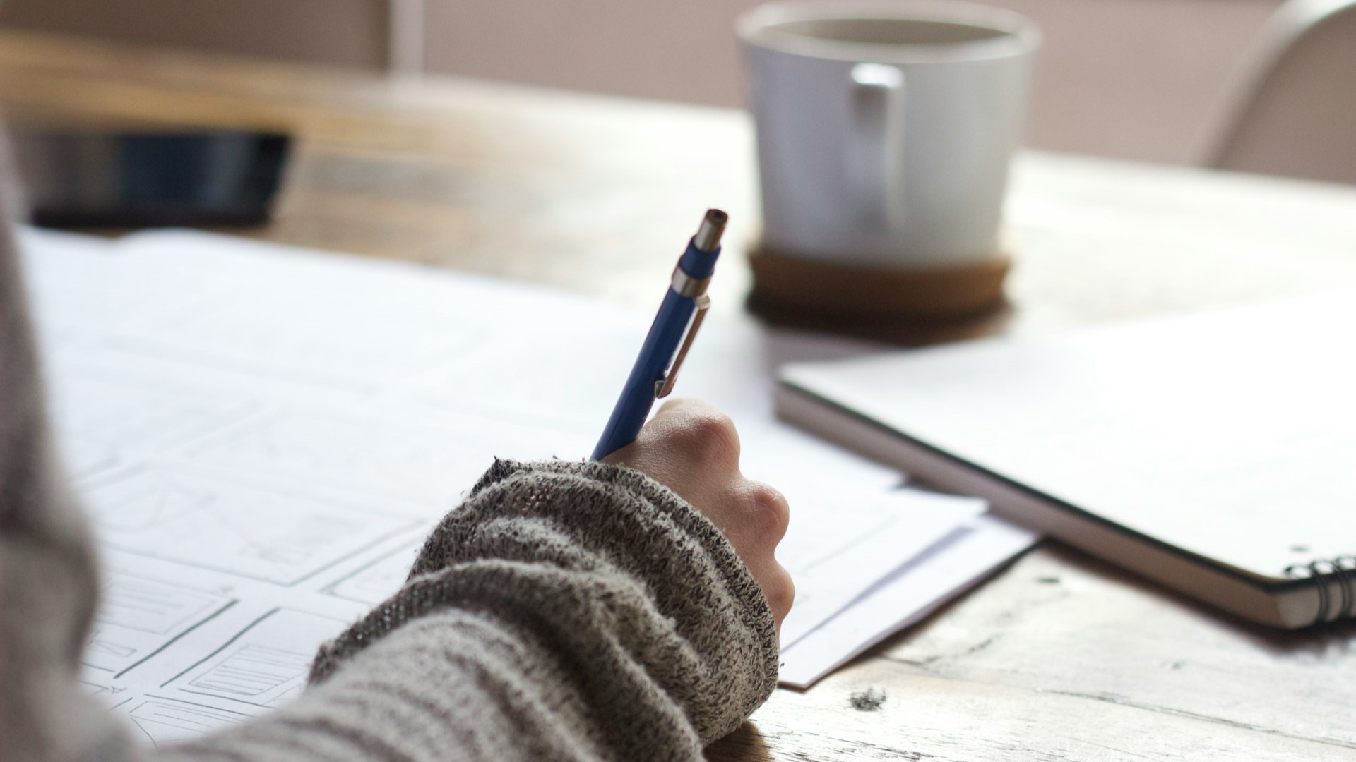 Persoon maakt aantekeningen op papier tijdens studie voor vavo, met pen en koffiemok op tafel