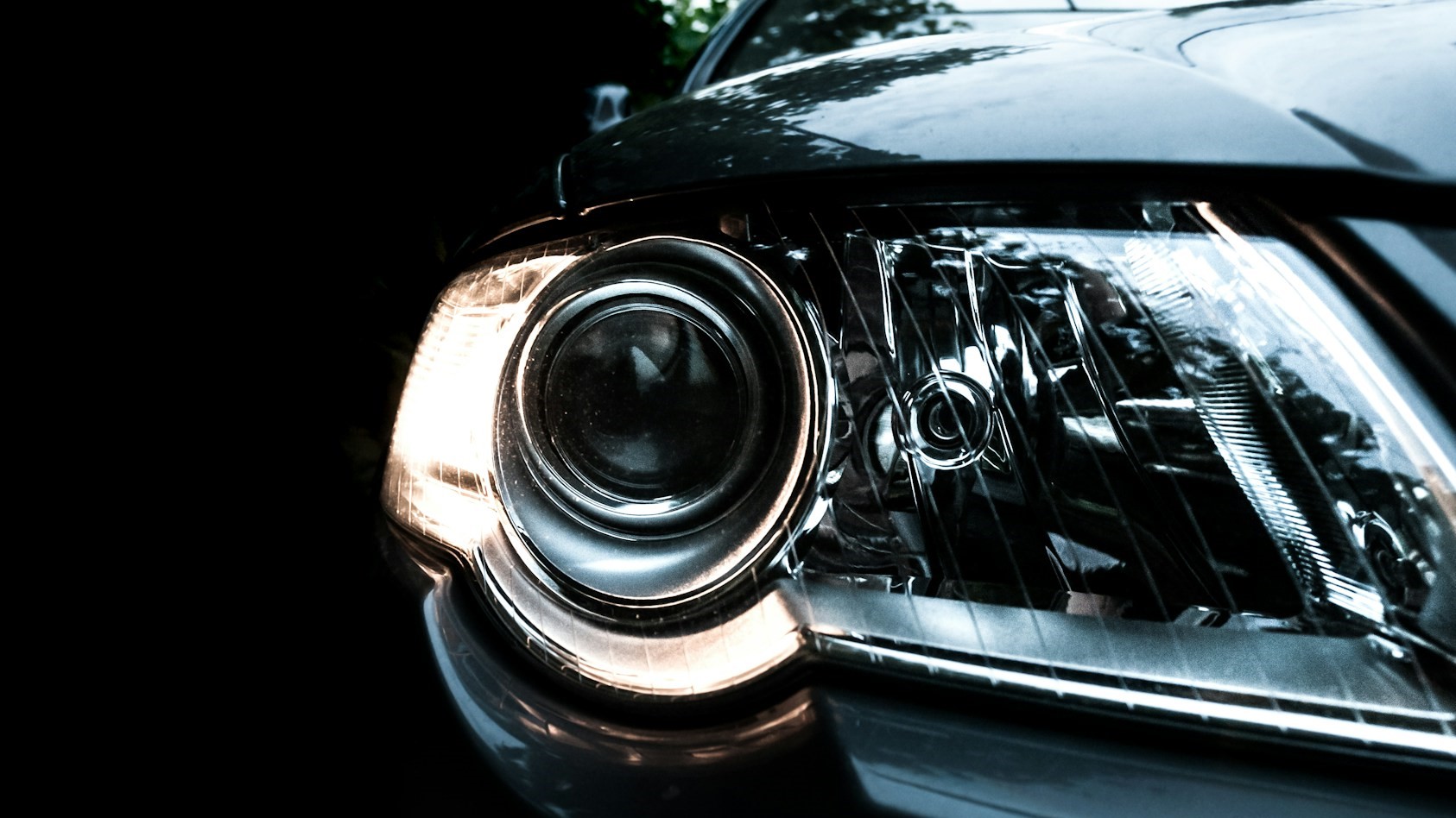 Close-up van een autokoplamp met ingeschakeld groot licht in een donkere omgeving