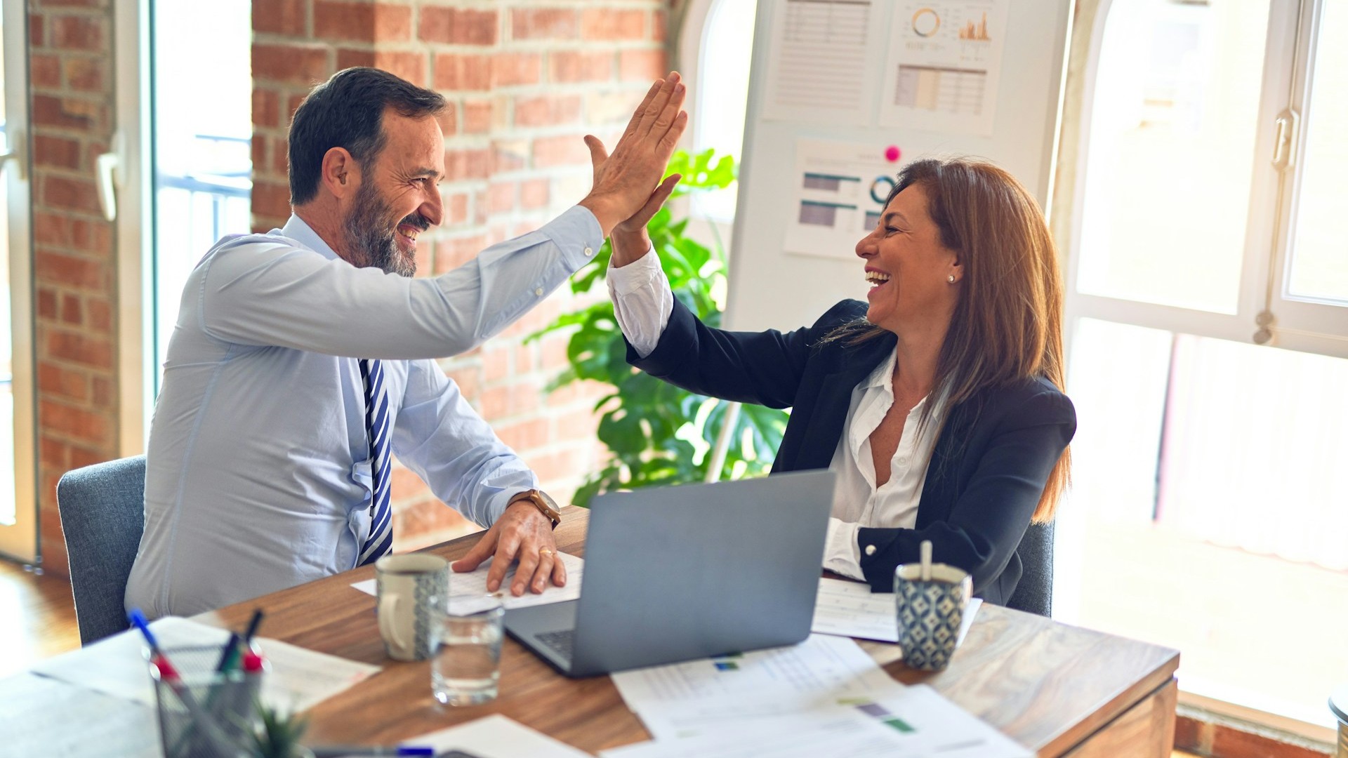 Twee personen geven elkaar een high five tijdens overleg, passend bij samenwerking binnen vertegenwoordiging geldzaken