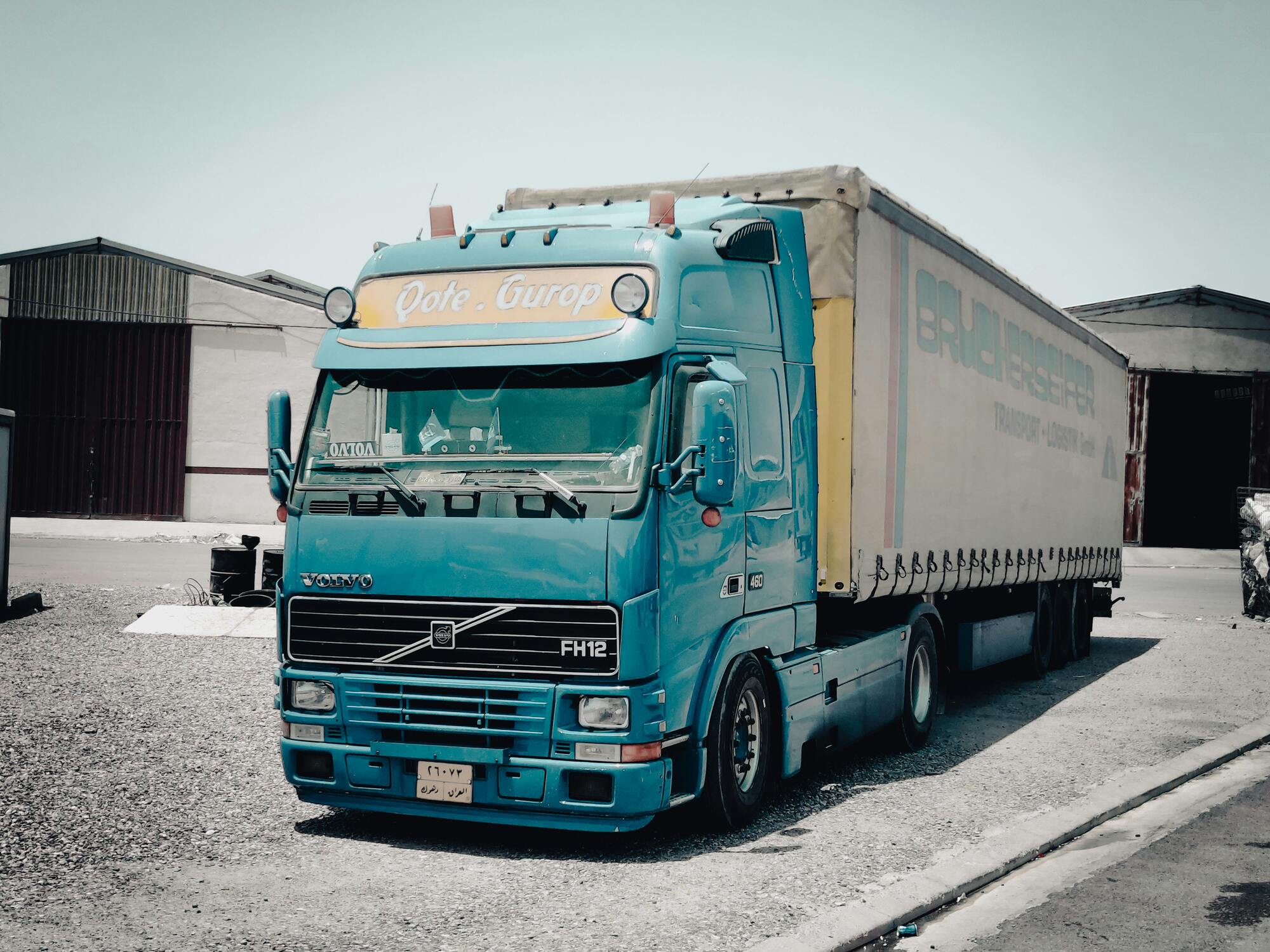 Turquoise vrachtwagen staat geparkeerd op industrieterrein met oplegger