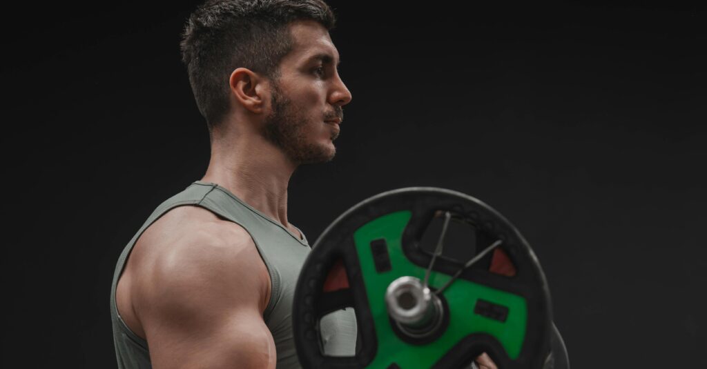 man met grijze top die sport met barbell met gewichten erop